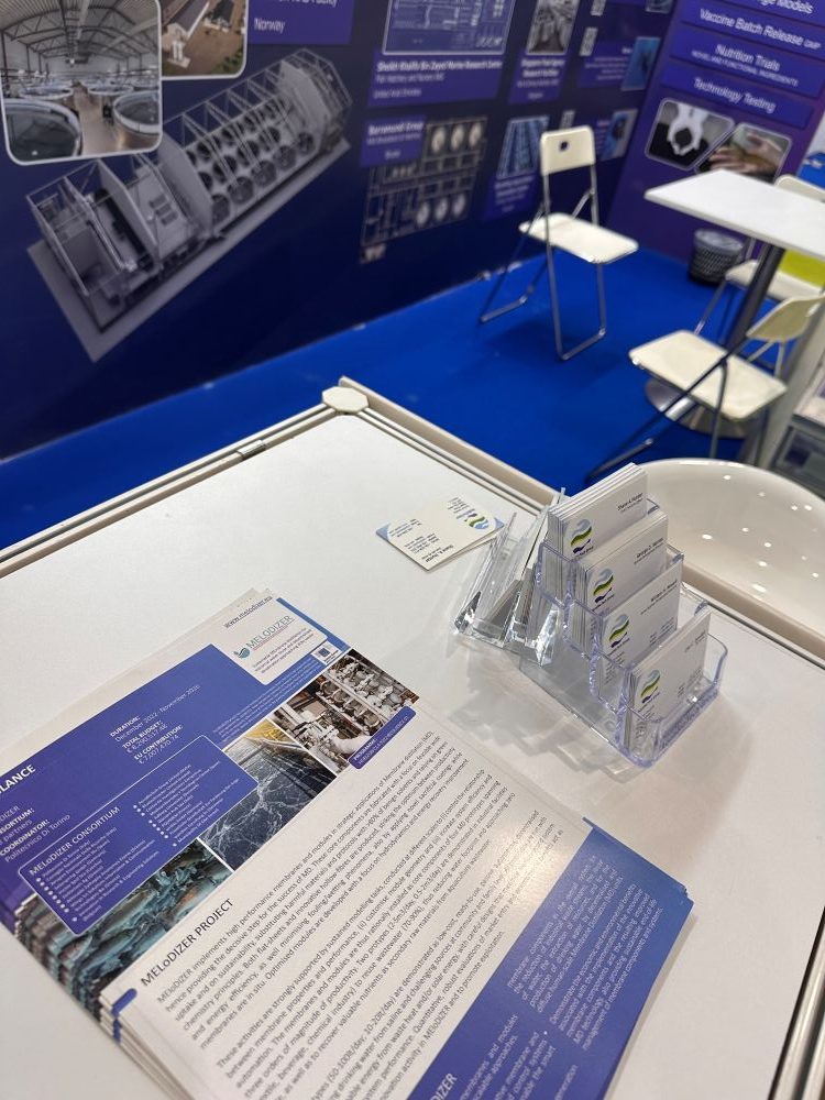 melodizer-aquabiotech-world-aquaculture-2026 AquaBioTech representative at the MEloDIZER booth during World Aquaculture 2026 in Singapore, with project brochures and dissemination materials on display.
